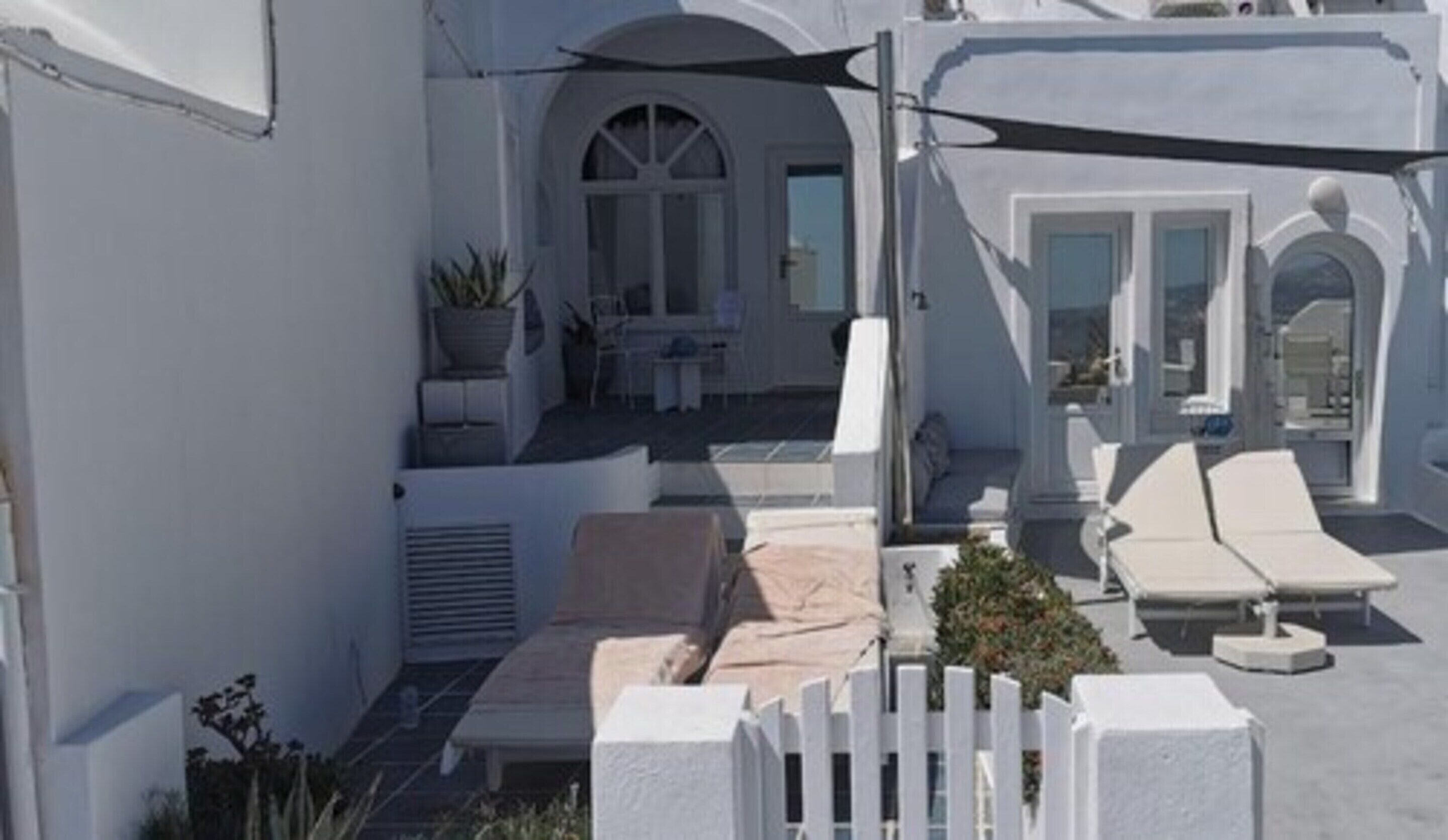 A white building with a covered outdoor seating area, a small table, and a potted plant.