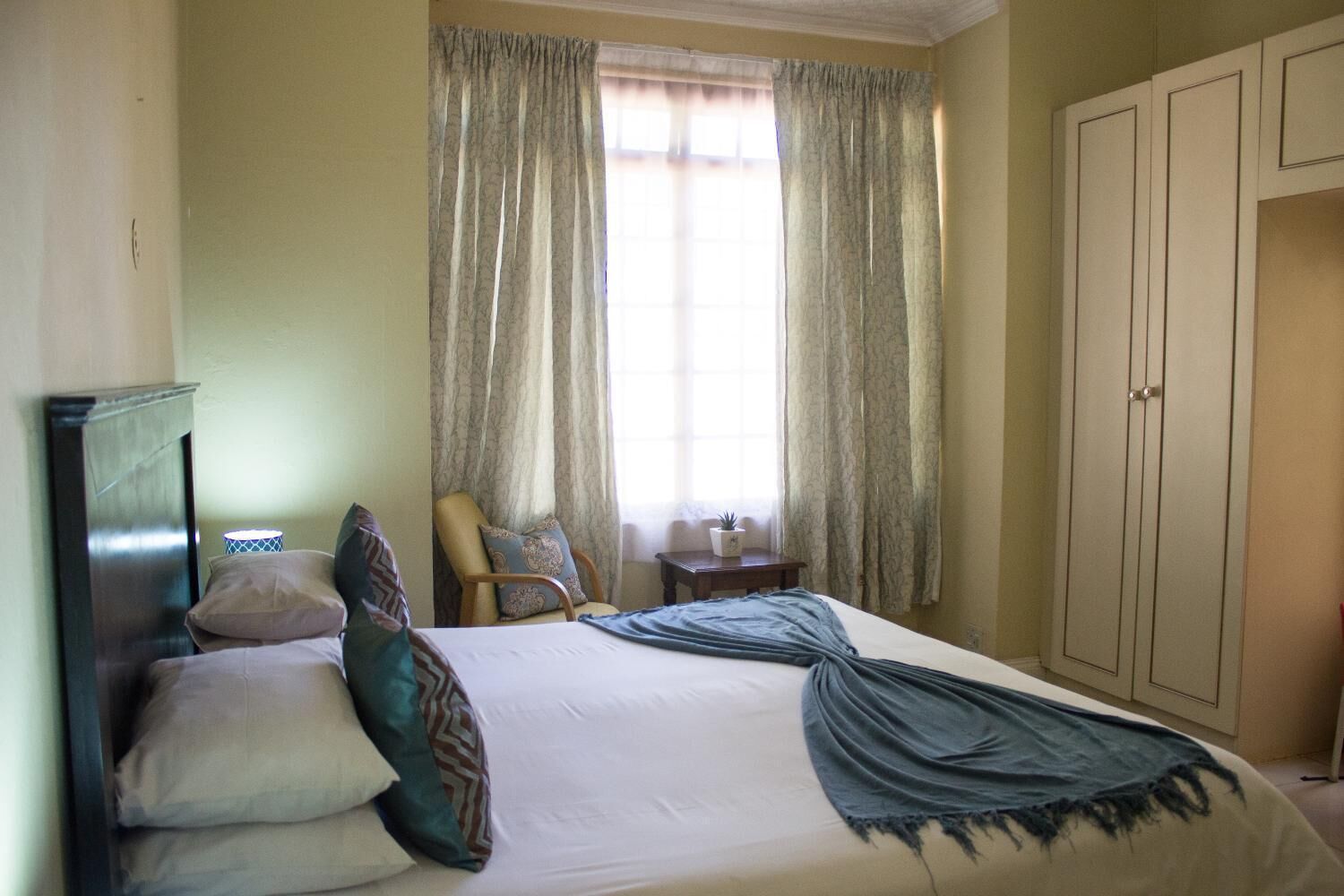 Una habitación de hotel con una cama, una silla, una mesita y un armario.