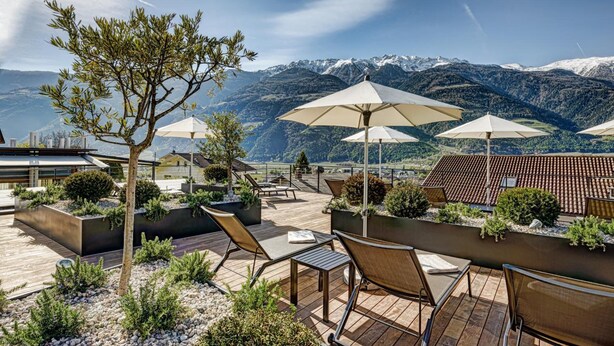 A rooftop terrace with outdoor seating, umbrellas, and a view of snow-capped mountains. - Boutique Hotel Belvedere (Naturno)