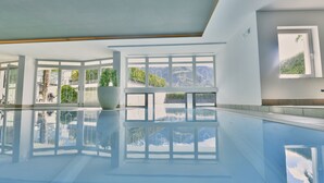A large indoor swimming pool with clear glass walls, a white ceiling, and a potted plant. - Boutique Hotel Belvedere (Naturno)