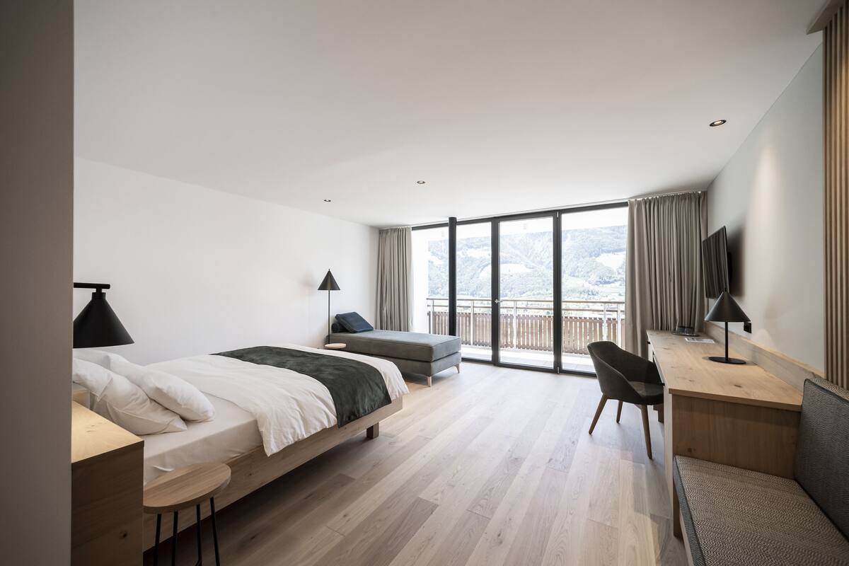Una habitación de hotel moderna con una cama grande, un escritorio, una silla y un balcón con vistas.
