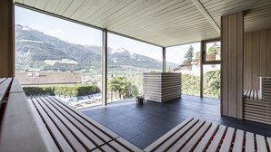 A modern interior with large windows, a wooden bench, and a stack of books. - Boutique Hotel Belvedere (Naturno)