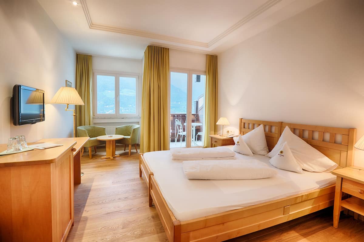 Habitación de hotel con cama de madera, escritorio con lámpara, una silla y vistas al exterior.