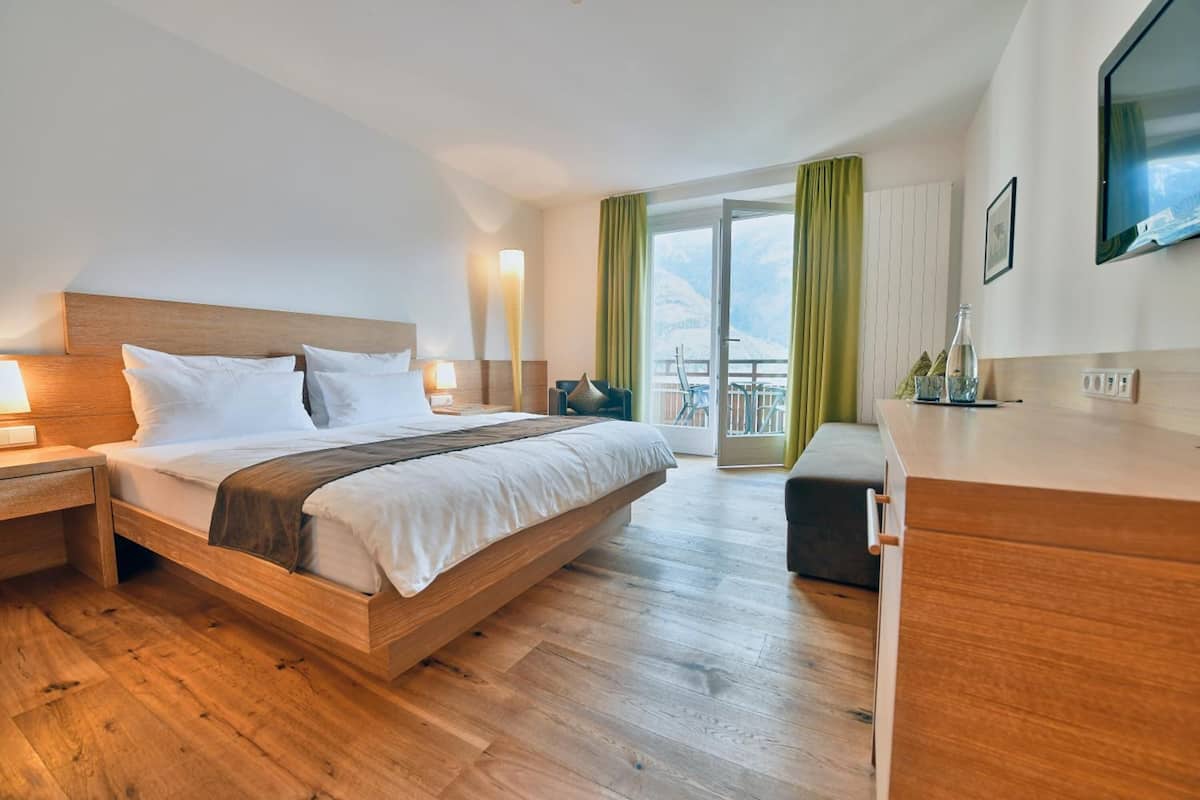 Habitación de hotel moderna con una cama de madera, una mesita de noche, un escritorio y vistas a montañas desde el balcón.
