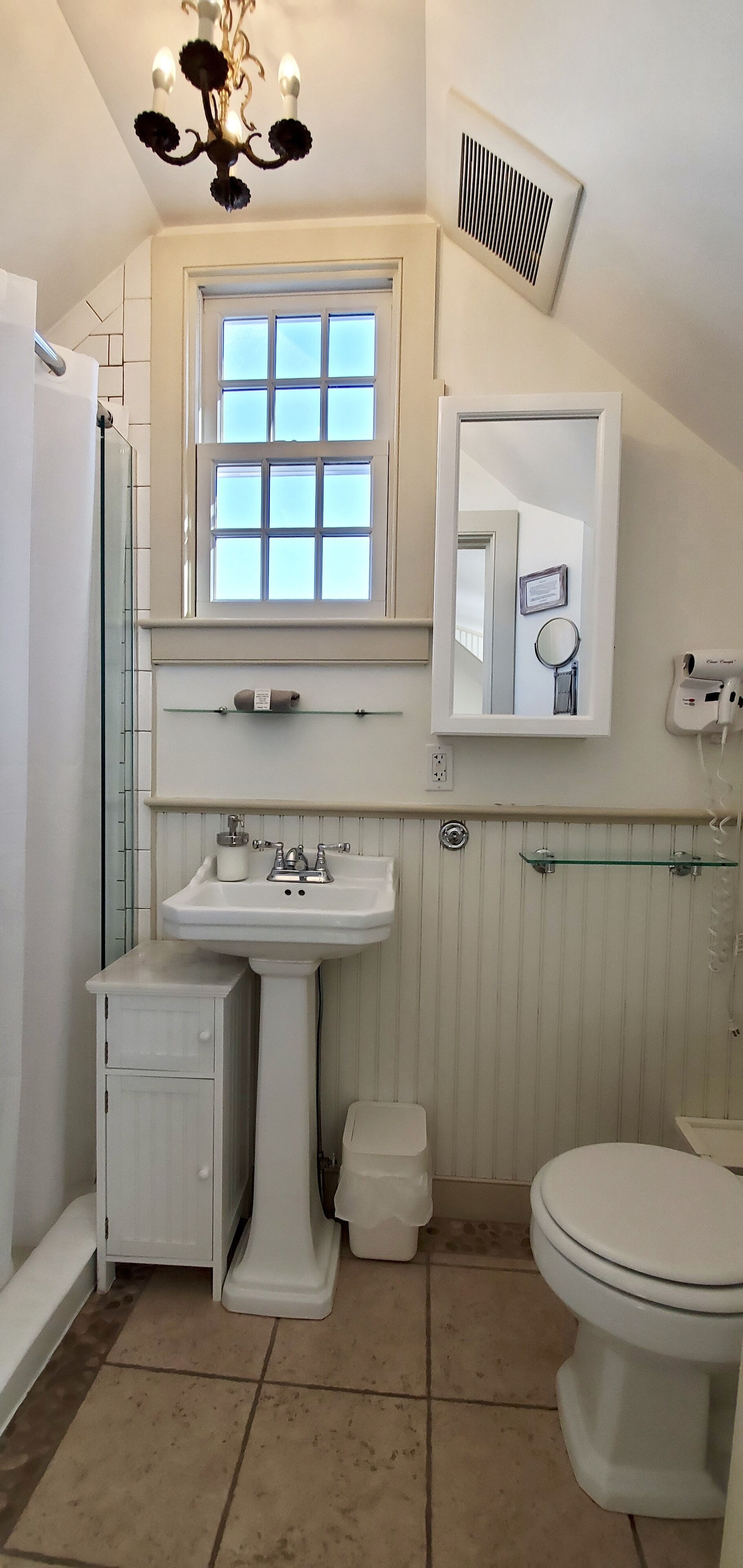 A bathroom with a pedestal sink, a toilet, a window, a mirror, and a shower.