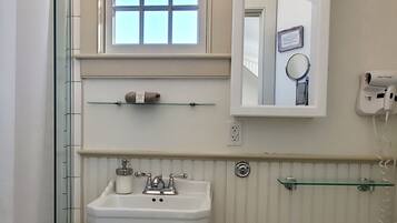 A bathroom with a pedestal sink, a toilet, a window, a mirror, and a shower.