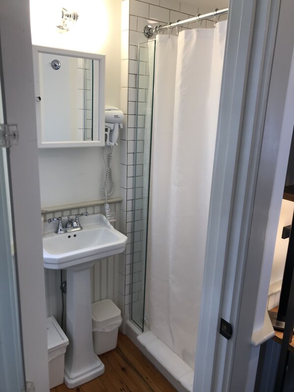 A bathroom with a pedestal sink, a handheld hair dryer, a glass shower enclosure, and a white toilet.