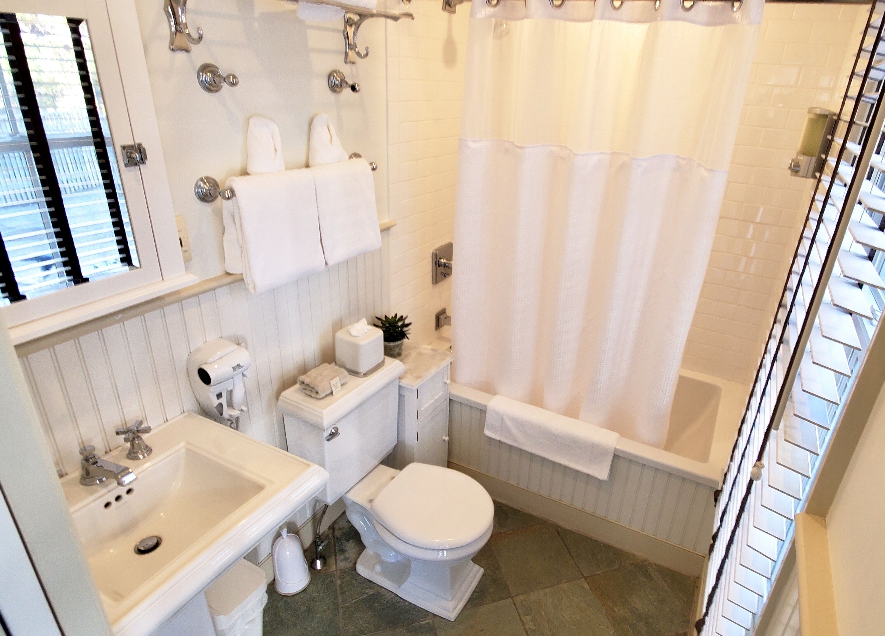 A bathroom with a toilet, sink, and bathtub. There are towels and a plant on the counter.