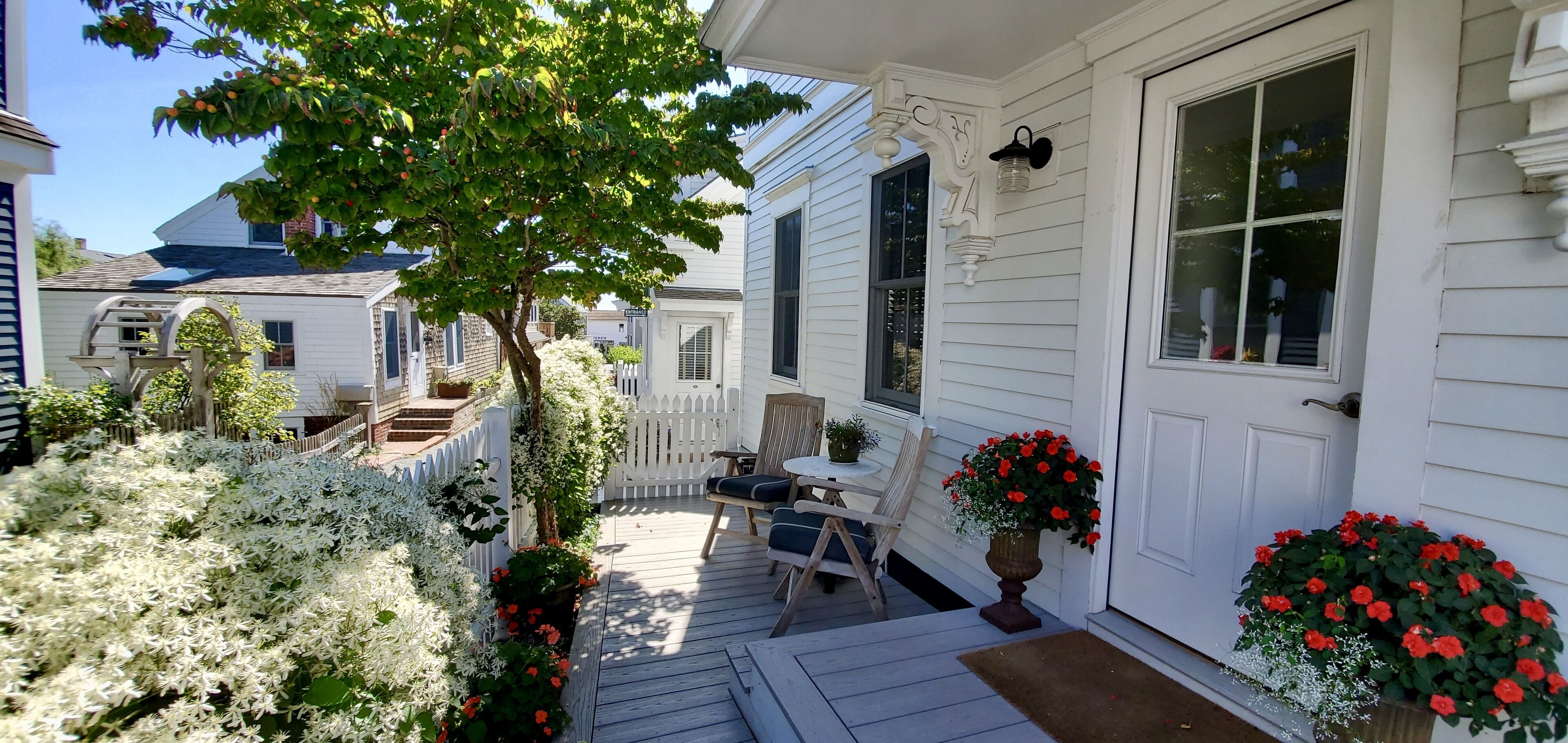 A white house with a porch, a dining table, chairs, and potted plants.