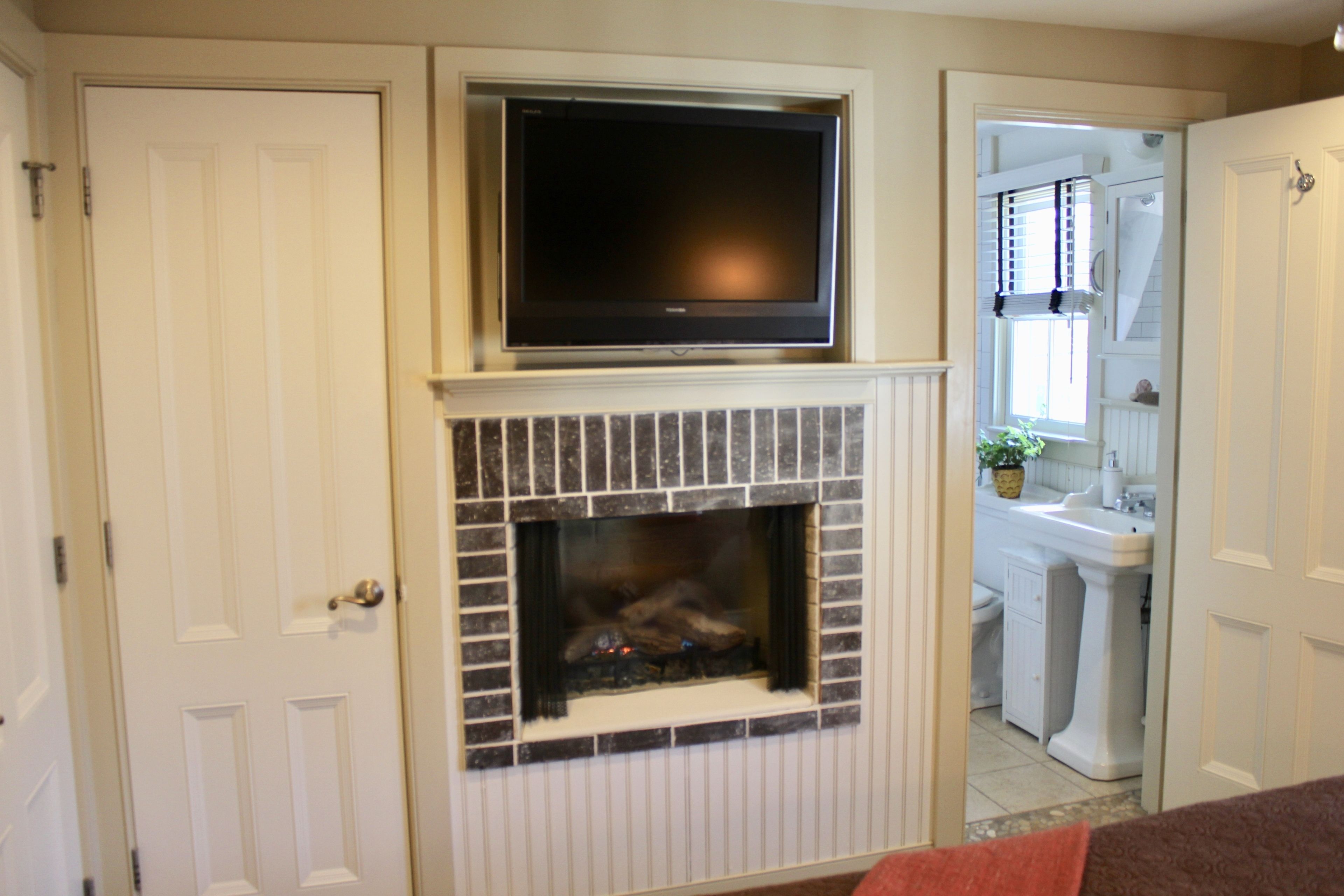 A room with a fireplace, a television mounted above it, and a door leading to another room.