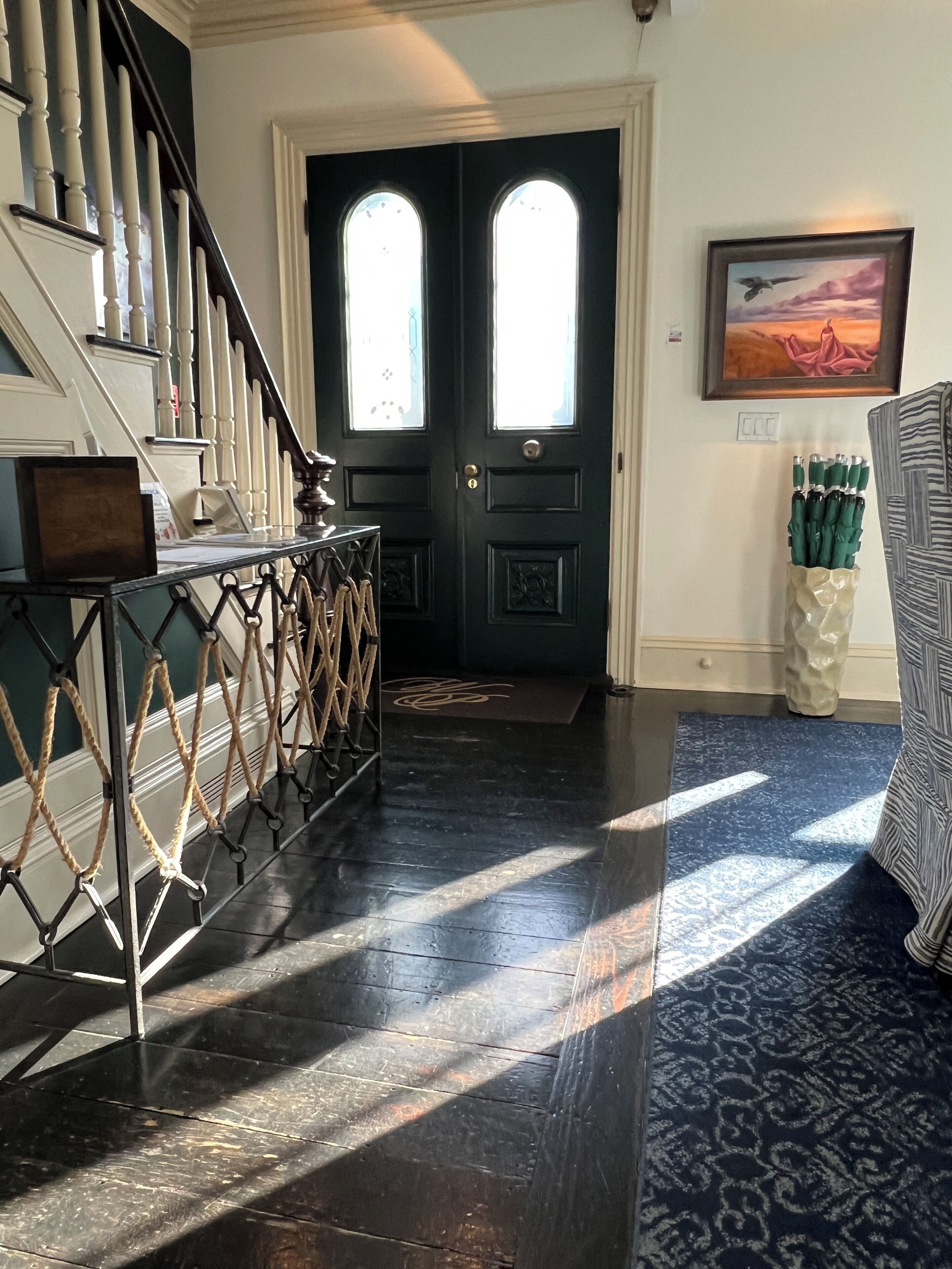 A staircase leading to a dark door with two windows, a doormat, and a wall-mounted picture.