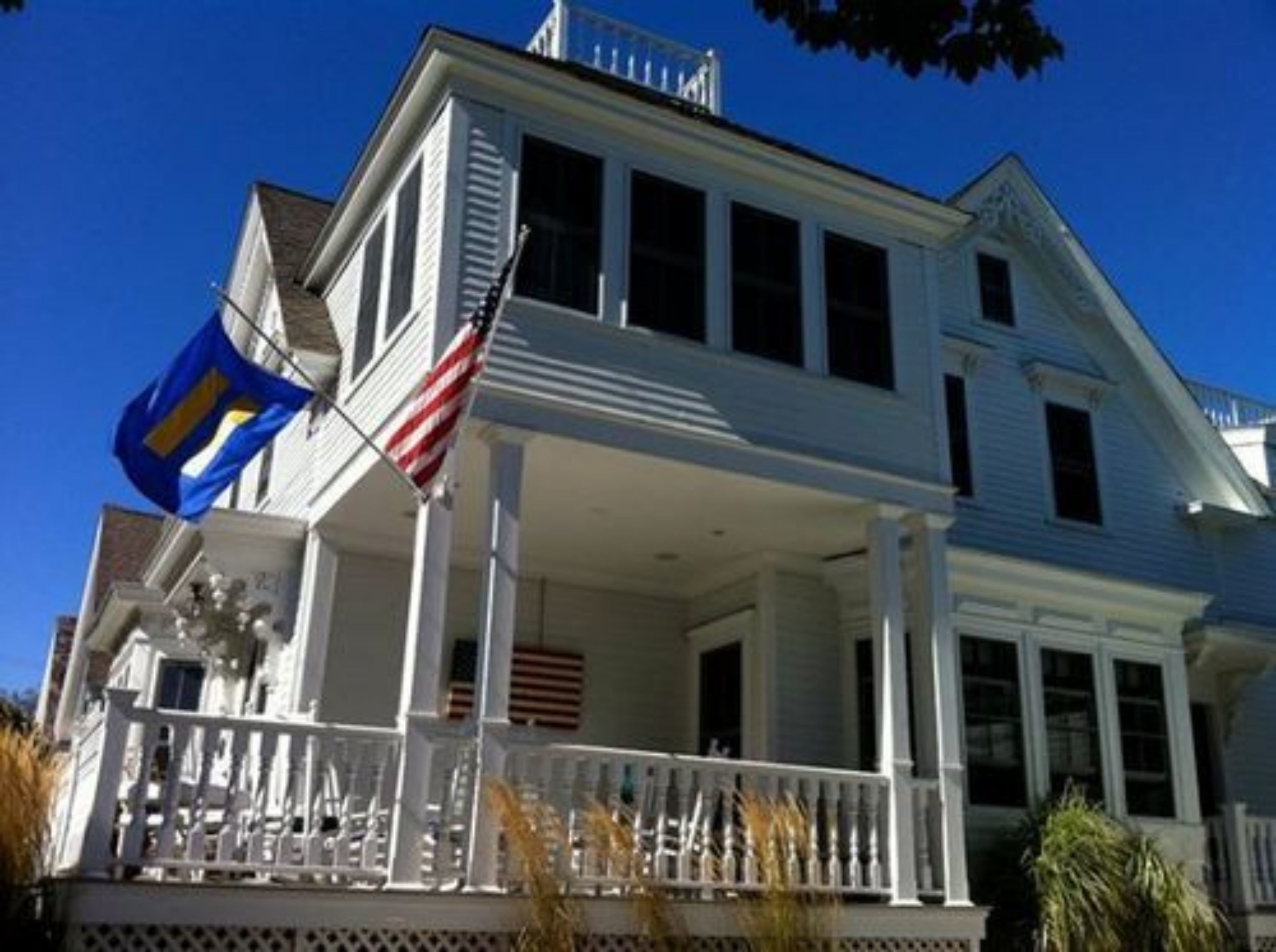 A two-story house with a porch, a flag, and a clear blue sky.