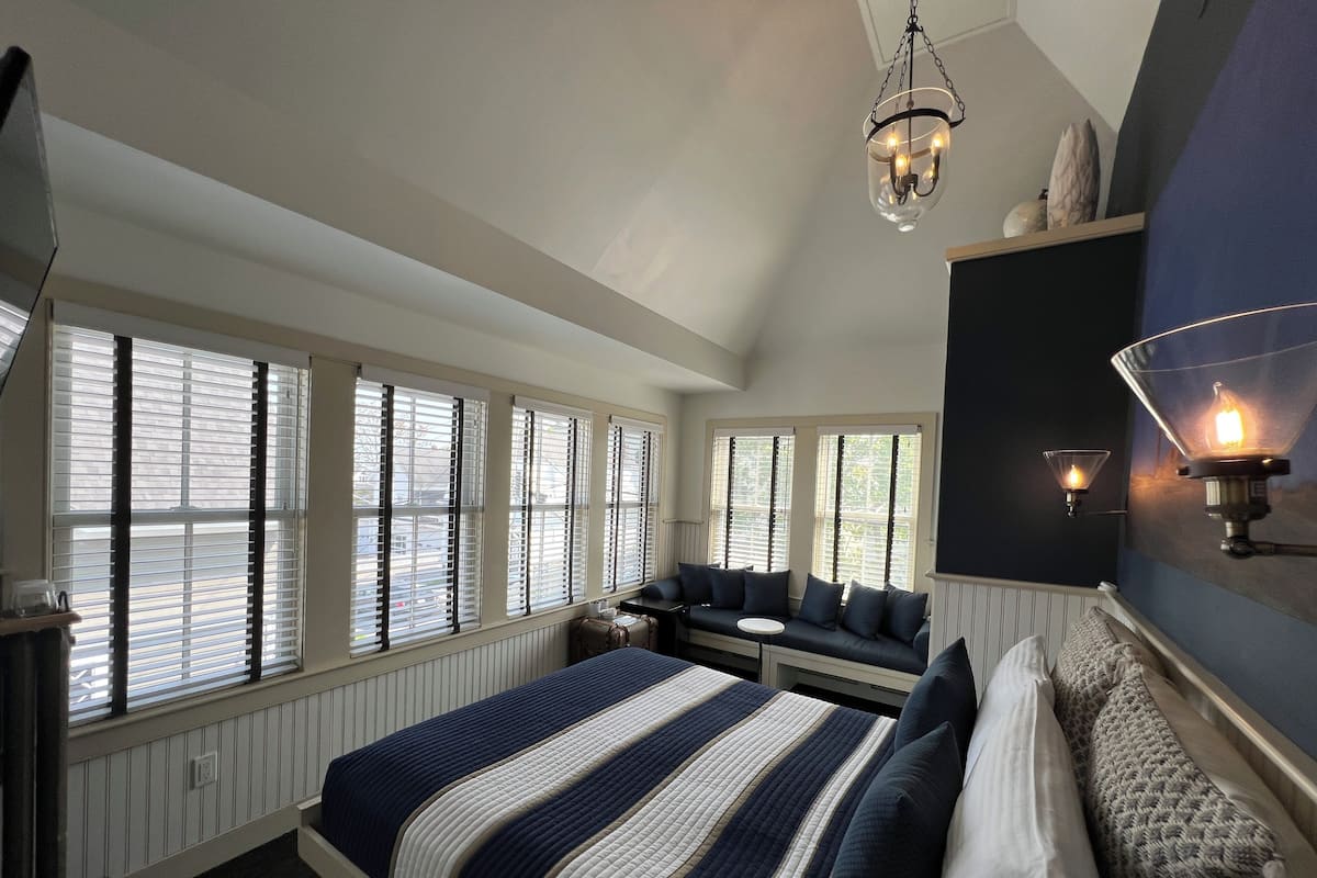 A bedroom with a large bed, a seating area, and a view through the windows.