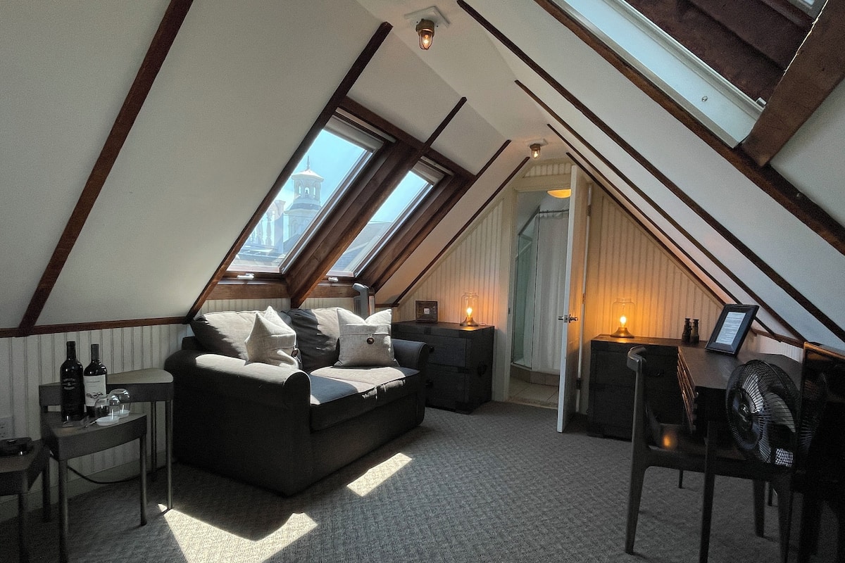 A cozy attic bedroom with a sloped ceiling, a sofa, a small table, and a chair.