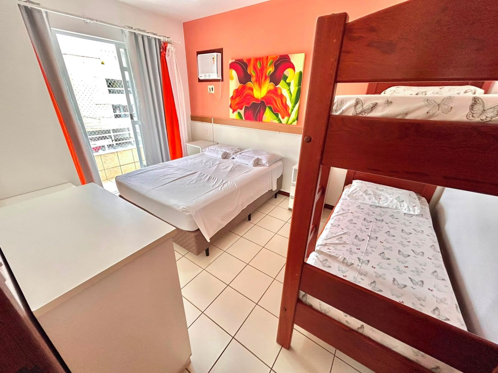 Ett hotellrum med en våningssäng, ett skrivbord, en stol, ett fönster med gardiner och en tavla på väggen.