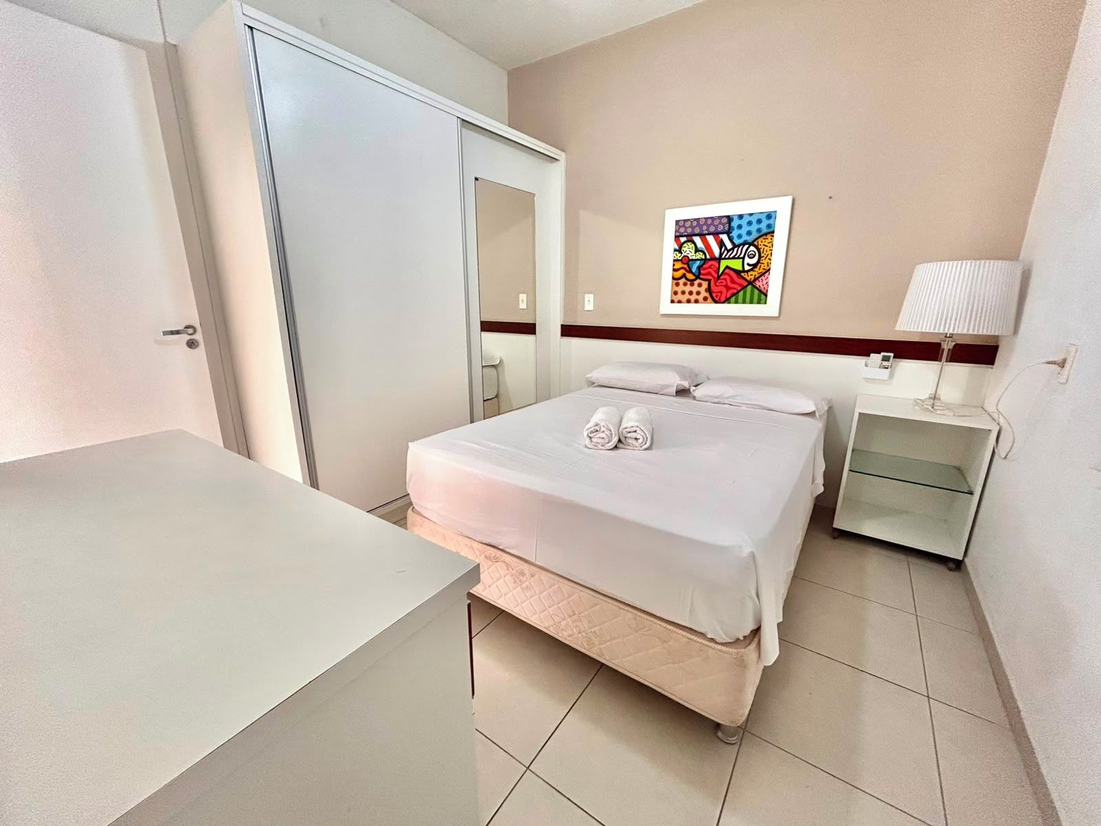 A hotel room with a bed, a bedside table, a lamp, and a wall-mounted artwork.