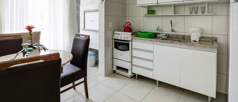 A compact kitchen with white cabinets, a stove, and a sink. There is a dining table with chairs and a potted plant.