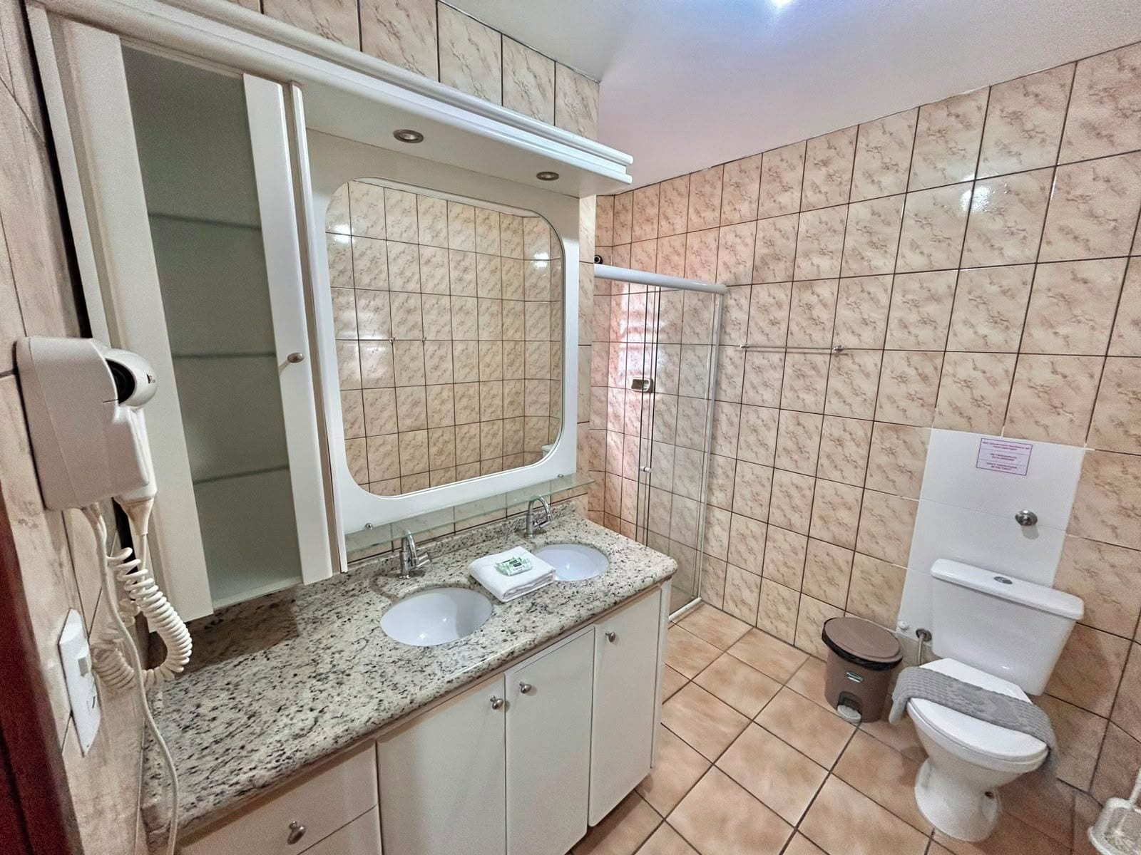 Un baño con lavamanos doble, inodoro, ducha y teléfono.