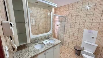 Un baño con lavamanos doble, inodoro, ducha y teléfono.