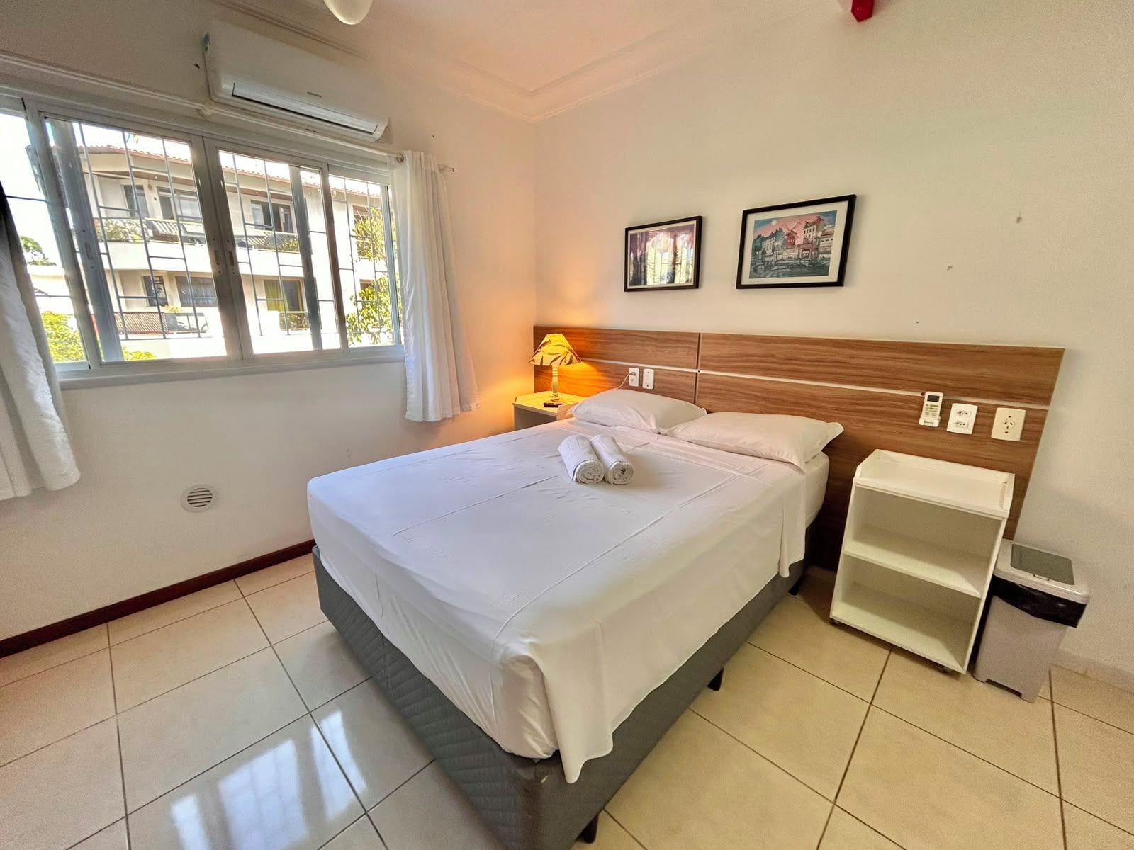Una camera d'albergo con un letto, una lampada da comodino, un comodino e una finestra con tende.