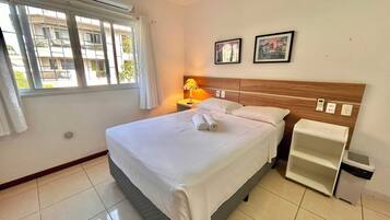 Una habitación de hotel con cama, lámpara de noche, mesita de noche y ventana con cortinas.