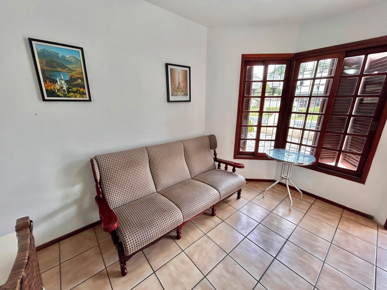 A room with a patterned sofa, a small round table, and two framed pictures on the wall.