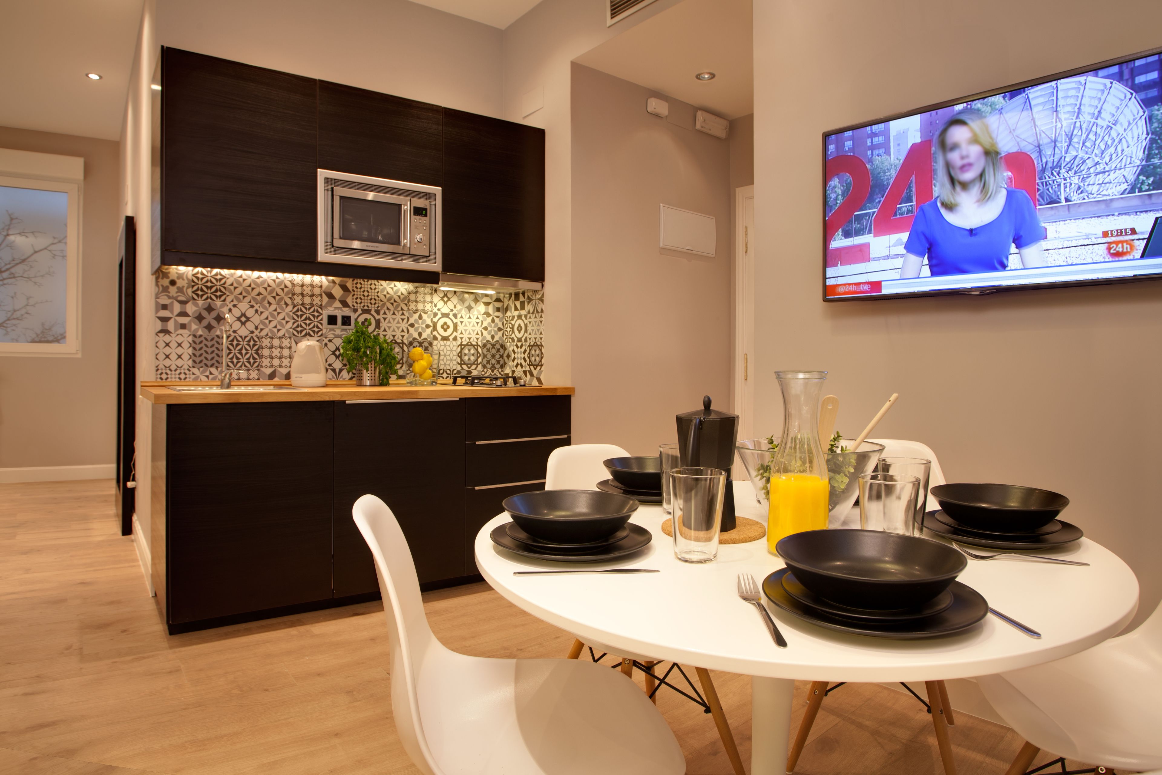 A modern kitchen with dark cabinetry, a microwave, and a tiled backsplash. A dining table with black plates and bowls is set for four.
