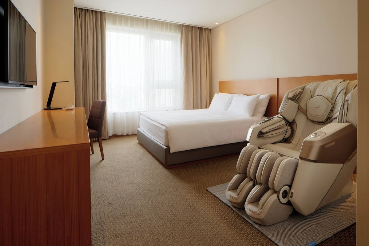 Quarto de hotel com uma cama, cadeira de massagem, escrivaninha e televisão.