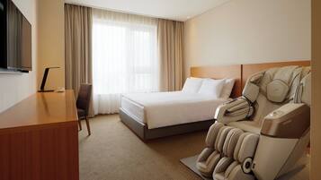 Ett hotellrum med en säng, en massagefåtölj, ett skrivbord och en TV.