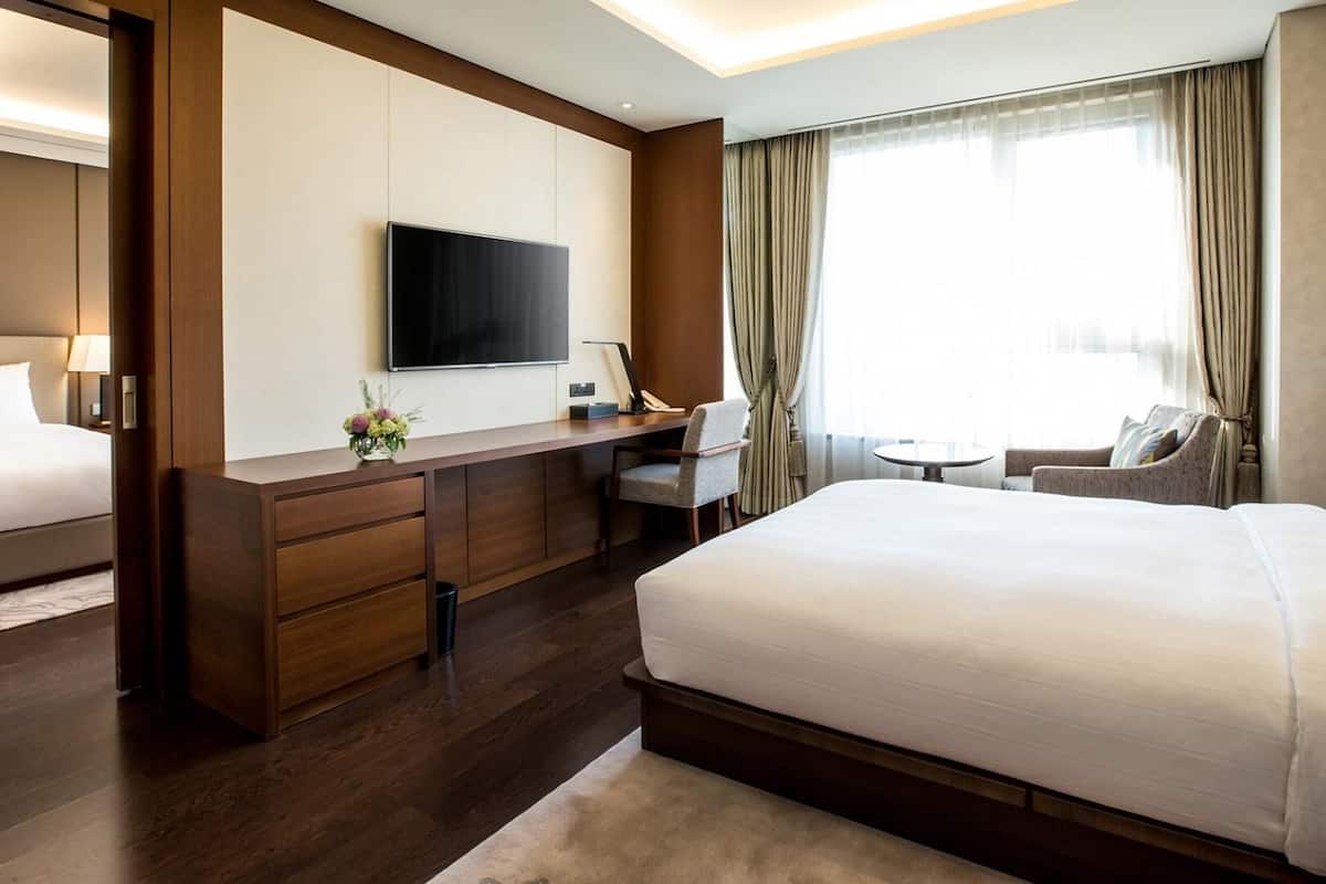 Quarto de hotel moderno com uma cama grande, uma escrivaninha com televisão de tela plana, uma mesinha e um sofá.