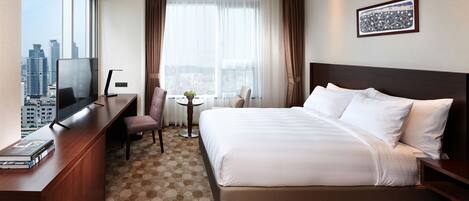 Habitación de hotel con una cama grande, un escritorio con televisor, una mesita con planta y vista a la ciudad.