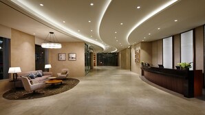 A modern hotel lobby with a curved ceiling, a reception desk, seating area with a sofa and chairs, and a large window providing a view. - LOTTE CITY HOTEL ULSAN (Ulsan)