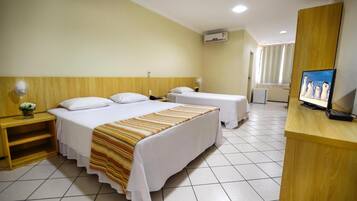 Quarto de hotel com duas camas, uma escrivaninha, uma televisão e uma janela com cortinas.