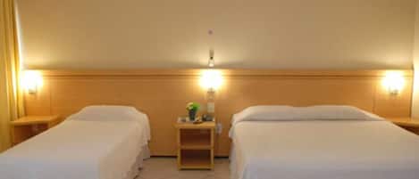 Habitación de hotel con dos camas individuales, una mesita de noche entre ellas y una pequeña mesa con lámpara.