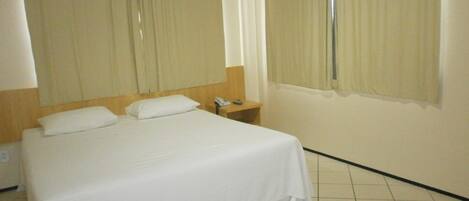 A hotel room with a single bed, a bedside table, and a window with curtains.
