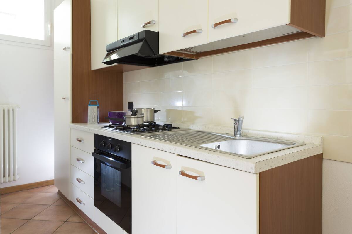 A compact kitchen with white cabinets, a stainless steel sink, and a built-in oven.