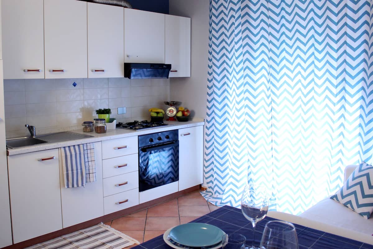 A kitchen with white cabinets, a stove, and a sink. There is a window with blue and white curtains.