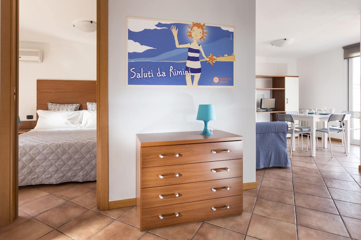 A hotel room with a bed, a wooden dresser, a desk with a computer, and a dining area with chairs and a table.