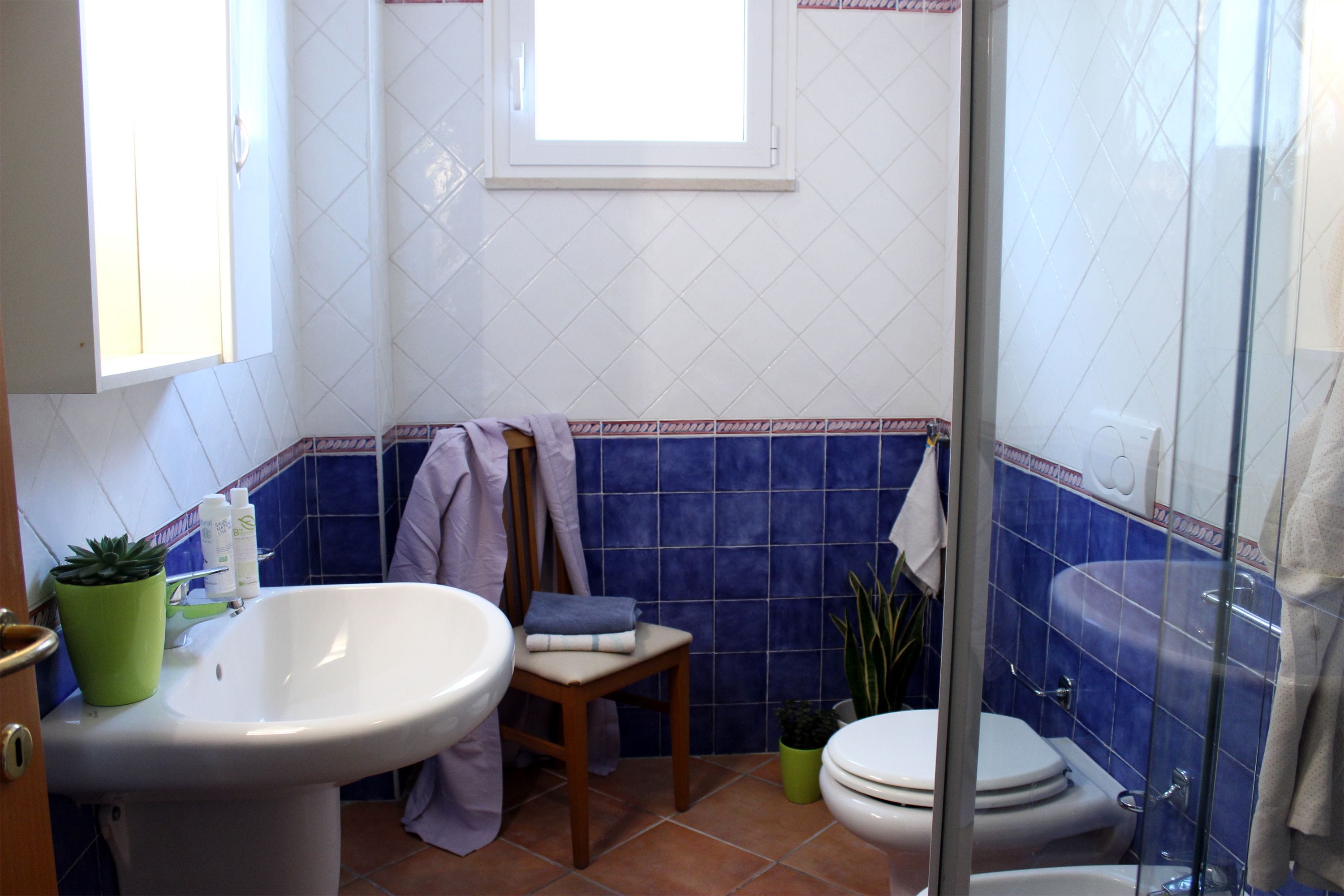 Une salle de bain avec un lavabo blanc, des toilettes, une douche et une fenêtre.