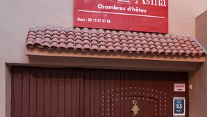 A closed wooden door with a brass knocker, a red sign above it, and a tiled roof. - Riad Asma (Taroudant)