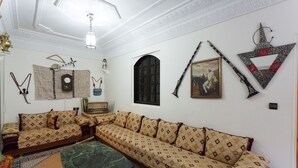 A living room with a sofa set, a clock, a framed picture, and wall decorations. - Riad Asma (Taroudant)