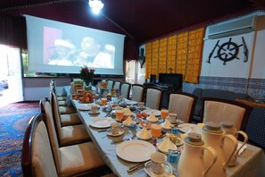 A dining area with a long table set for a meal, chairs, a projector screen, and a wall with a decorative item.