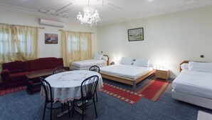 A hotel room with two single beds, a red sofa, a dining table with chairs, a chandelier, and a painting on the wall. - Riad Asma (Taroudant)