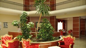 A lobby with red and gold chairs, a palm tree, and a reception desk. - Larissa Inn (Kemer)