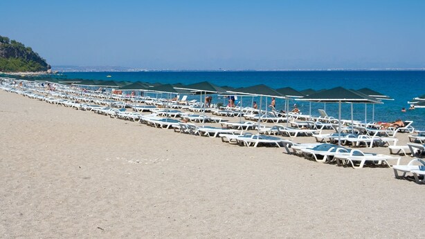 A beach with rows of sun loungers and umbrellas, a clear blue sky, and the sea in the background. - Larissa Inn (Kemer)