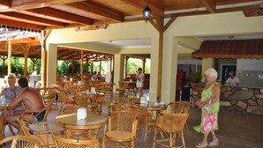 An outdoor dining area with wicker furniture and a stone wall in the background. - Larissa Inn (Kemer)
