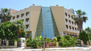 A multi-story hotel with a central glass facade, surrounded by palm trees and various plants. - Larissa Inn (Kemer)