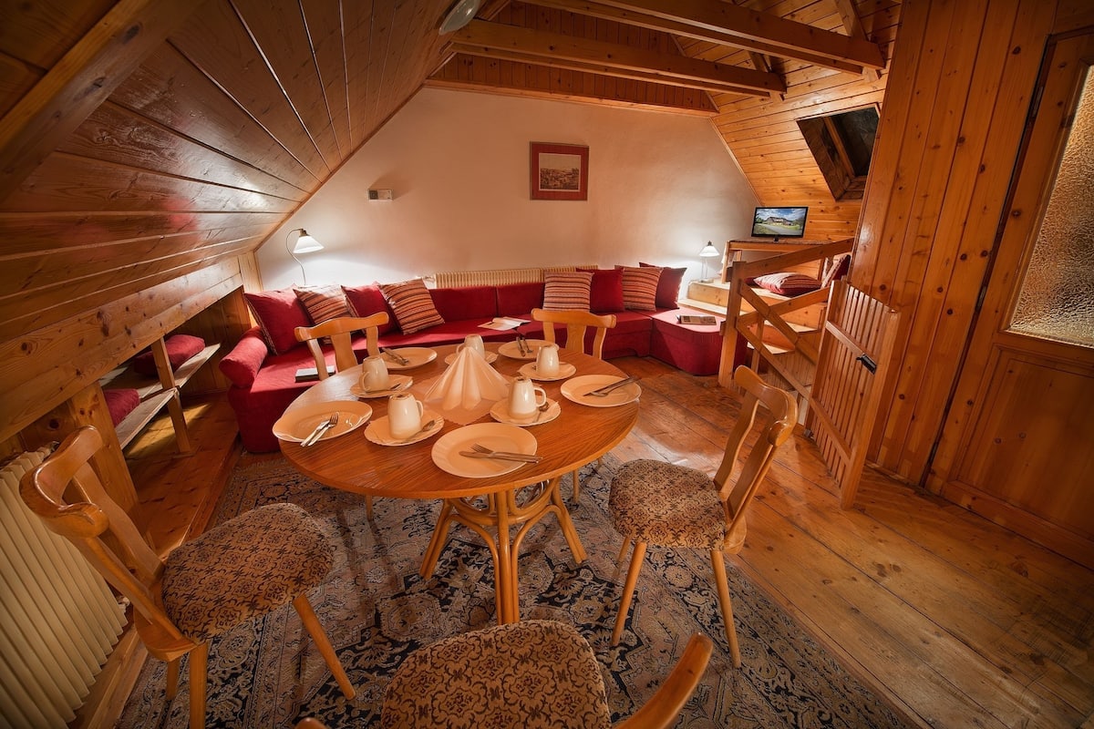 A cozy, wooden-furnished dining area with a round table set for four, surrounded by patterned chairs.