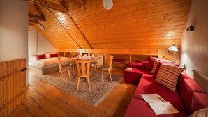 A cozy attic room with a wooden ceiling, a red sofa, a dining table with chairs, and a bed with red pillows. - Penzion Farma U Mauritzů (Stozec)