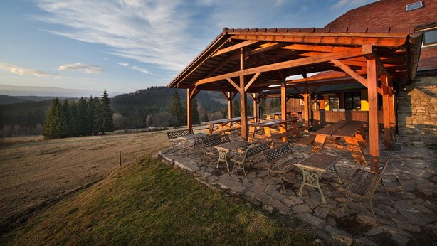 A covered outdoor seating area with stone flooring and metal furniture, overlooking a mountainous landscape. - Penzion Farma U Mauritzů (Stozec)